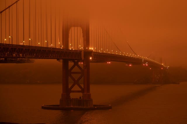 Cars drive along the San Francisco Bay Bridge under an orange smoke filled sky as more than 300,000 burn across California, including 35 major wildfires