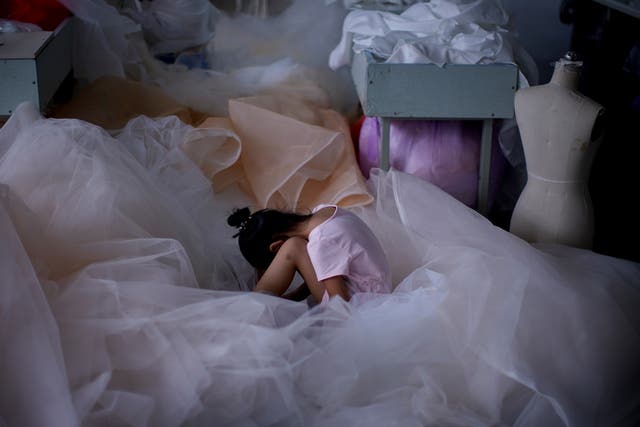 A girl sits on a piece of fabric as she plays on a mobile phone at a small wedding dress factory in July