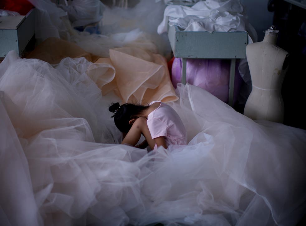 A girl sits on a piece of fabric as she plays on a mobile phone at a small wedding dress factory in July