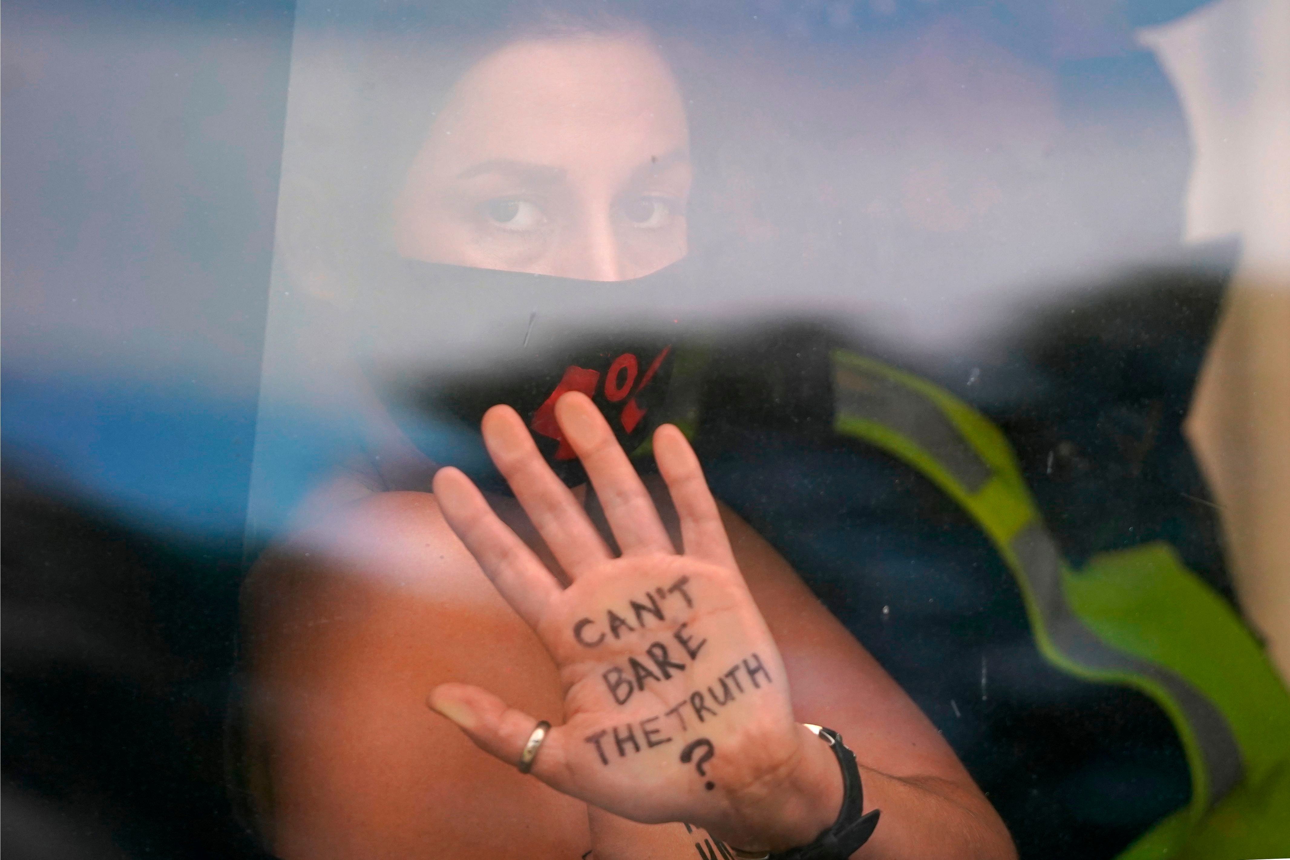 An activist from the Extinction Rebellion climate change group shows a message written on her hand as she is taken away in a police van
