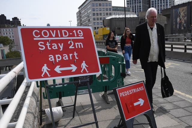 Pedestrians pass a social distancing sign on Waterloo Bridge in London
