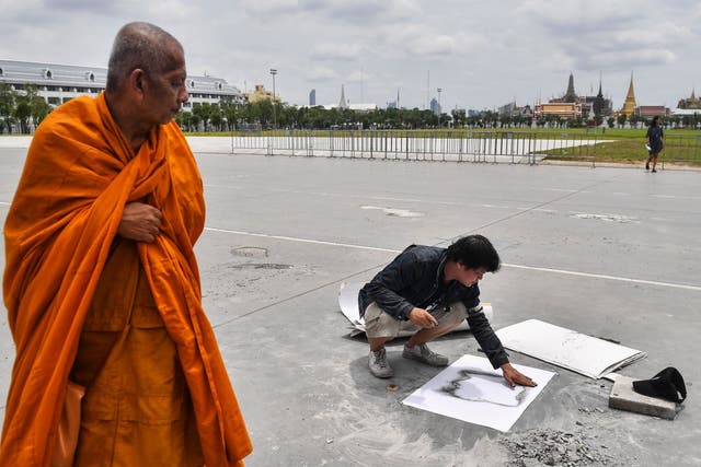 A monk watches as an art professor from Silpakorn University makes a stencil over an empty space in Bangkok where the commemorative plaque had been placed by pro-democracy protest leaders