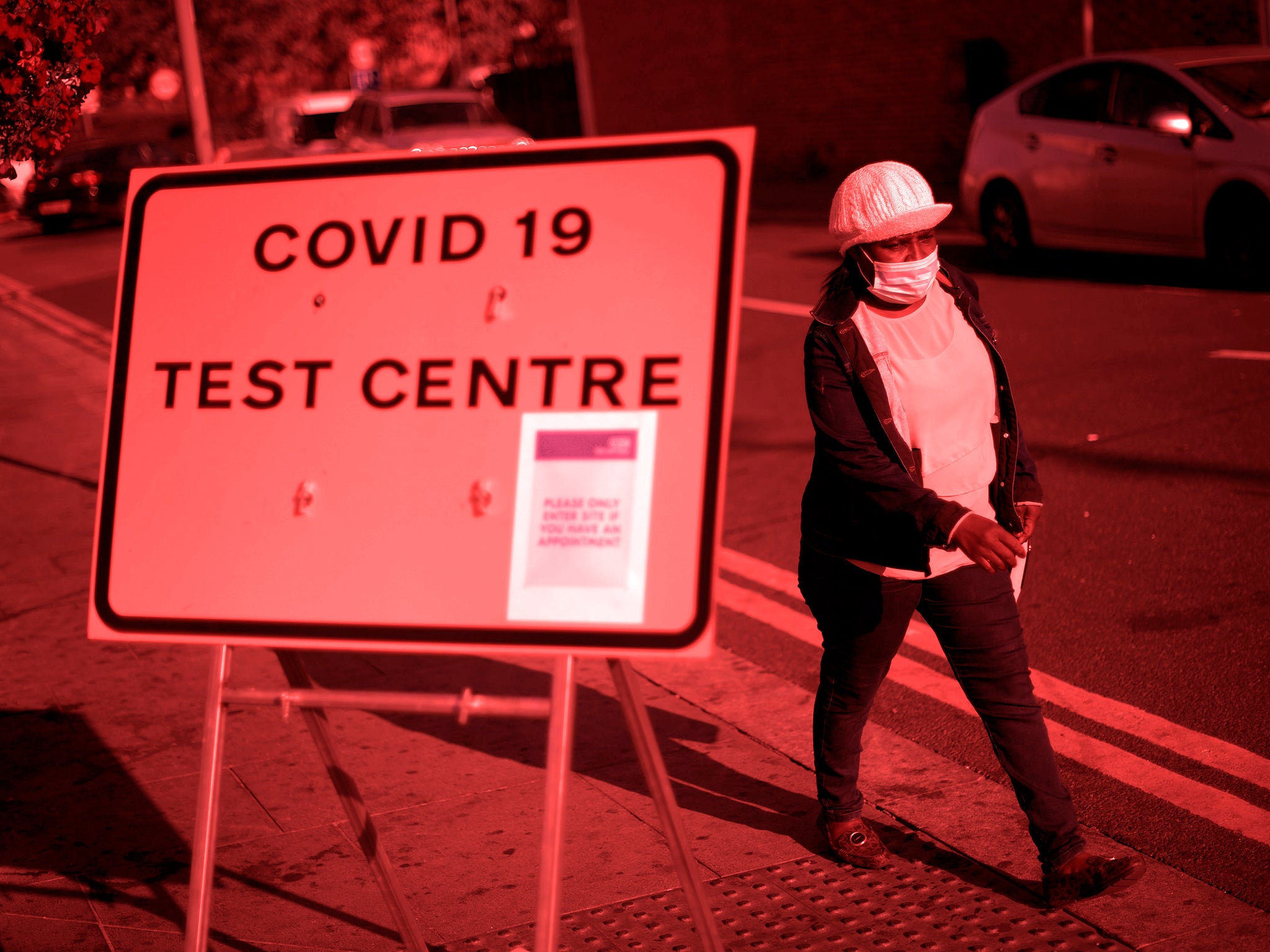 Pedestrian wearing facemask walks past a sign for a Covid-19 test centre in Leyton, east London on 19 September