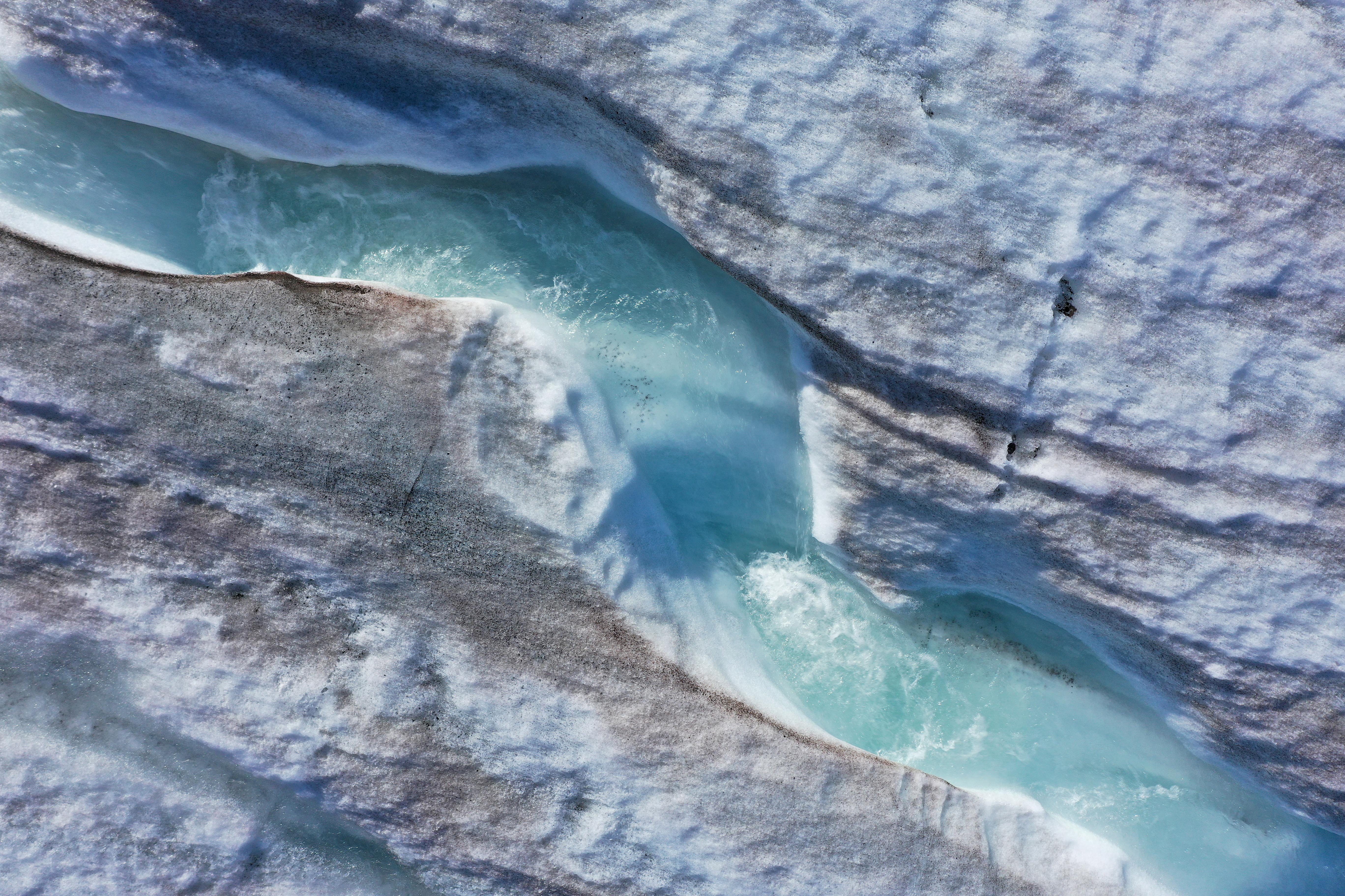 Water carves a winding channel down the surface of the melting Longyearbreen glacier during a summer heat wave on Svalbard archipelago
