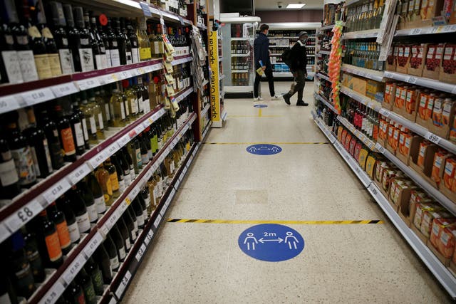 Floor stickers in the alcohol aisle inside a Tesco Metro supermarket ask customers to social distance as they shop