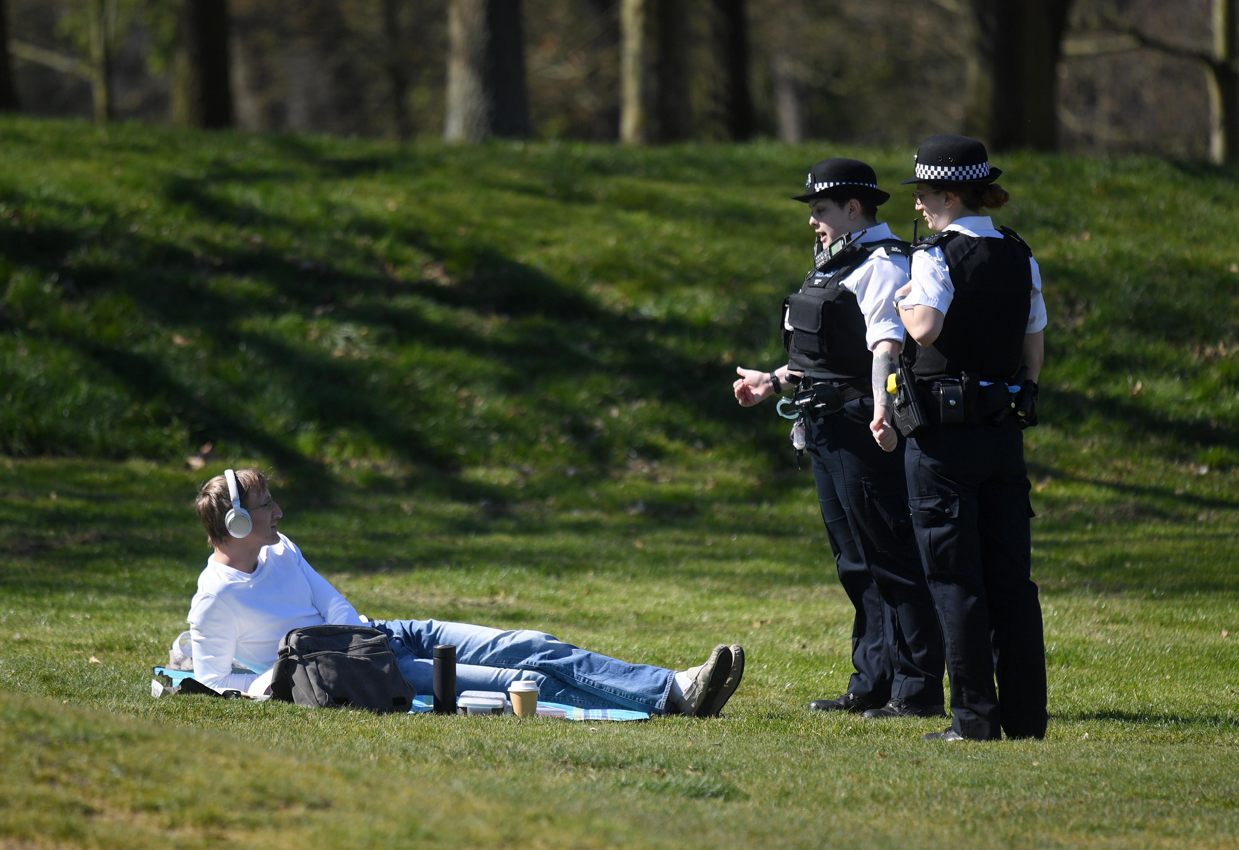 Police enforcing lockdown restrictions speak to a sunbather in a London park