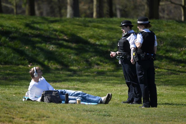 Police enforcing lockdown rules speak to a sunbather in a London park