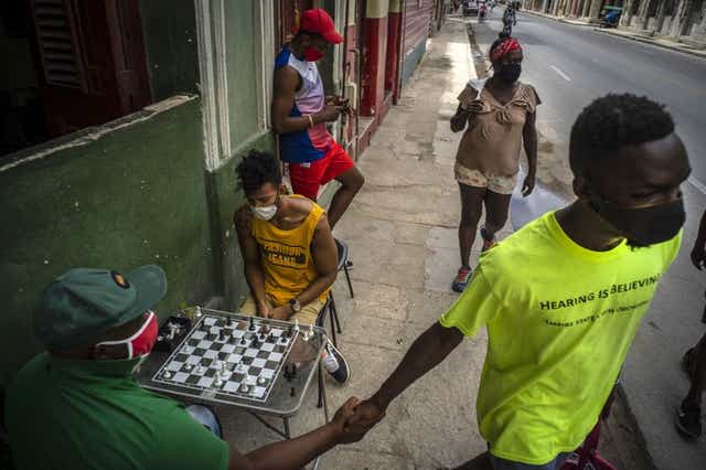 Personas con cubrebocas caminan por una calle mientras otros juegan al ajedrez en una acera en La Habana, Cuba, el miércoles 23 de septiembre de 2020. Estados Unidos agregó el lunes 28 de septiembre de 2020 a su lista negra para operar con Cuba a una tarjeta de débito que en los últimos meses se volvió popular en la isla. (AP Foto/Ramón Espinosa)