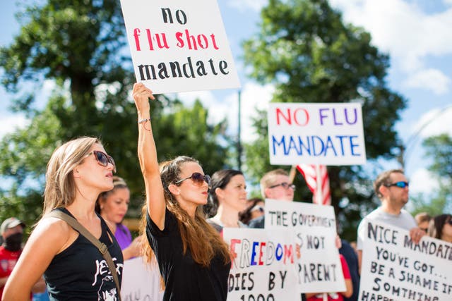 Anti-vaccine activists hold signs in front of the Massachusetts State House during a protest against mandatory vaccines
