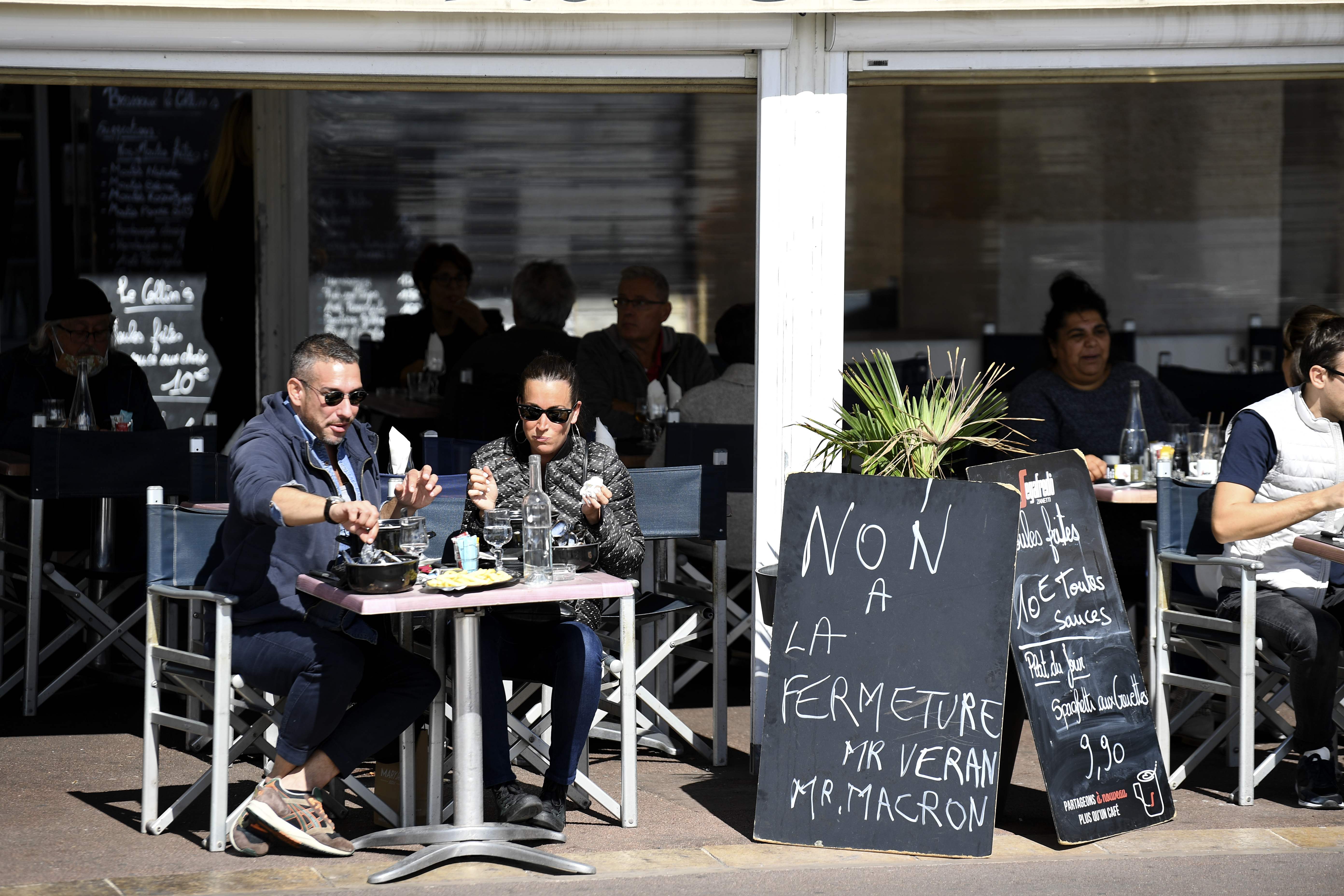 A couple have lunch in Marseille next to a sign reading ‘No to the shutdown, Mr Macron’