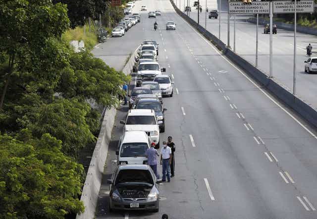 Varias personas se paran junto a vehículos alineados para ingresar a una estación de servicio durante una escasez de combustible en Venezuela.
