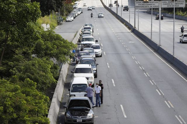 Varias personas se paran junto a vehículos alineados para ingresar a una estación de servicio durante una escasez de combustible en Venezuela.