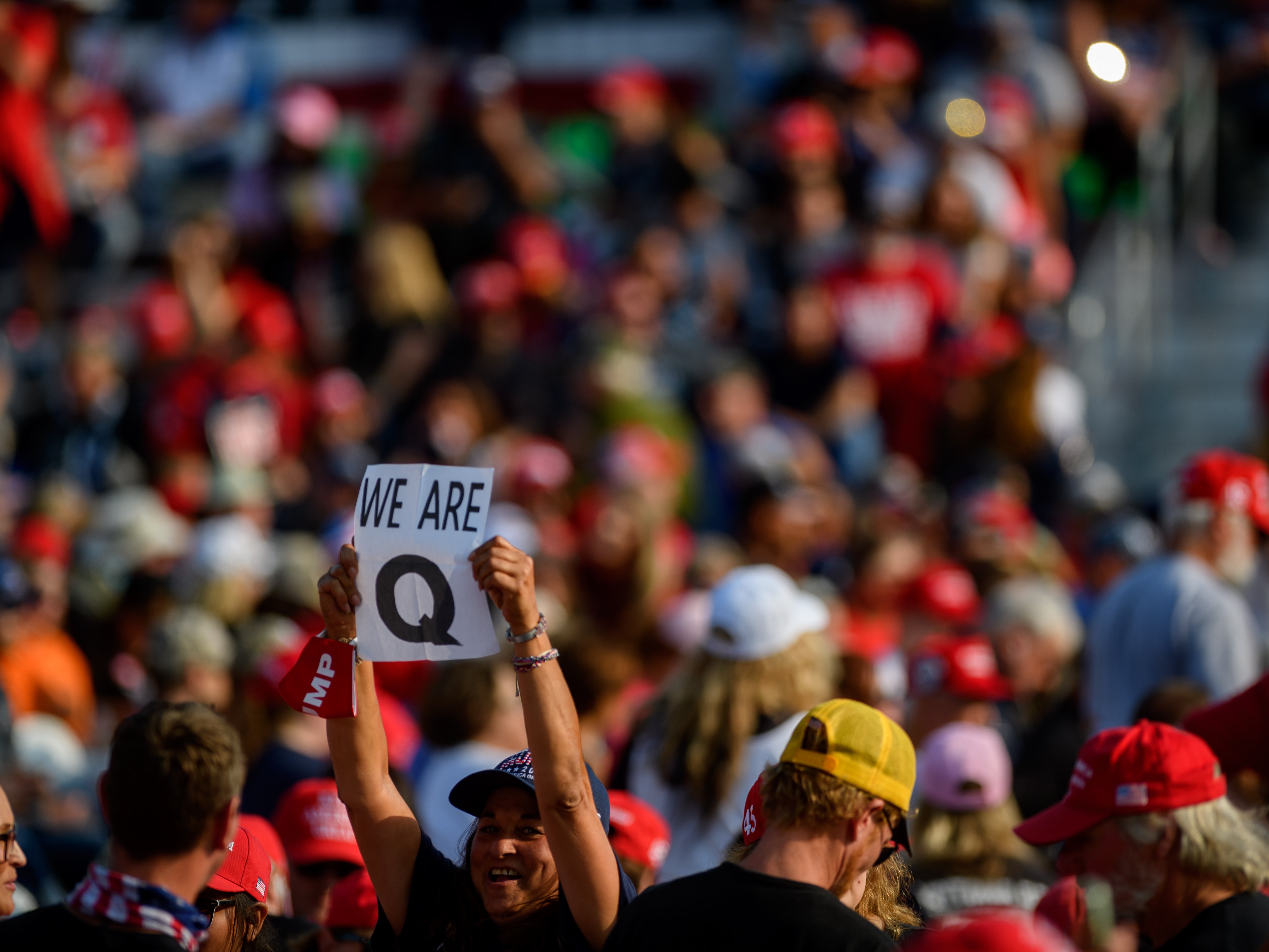 A woman holds up a QAnon sign to the media as attendees wait for President Donald Trump to speak at a campaign rally