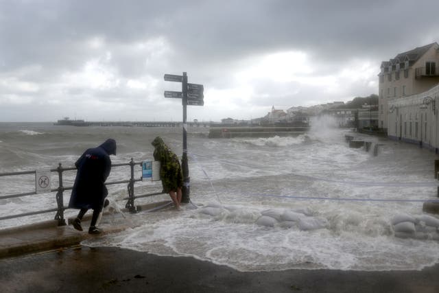 People watch as waves crash along the coast at Swanage in Dorset on Friday as Storm Alex hit