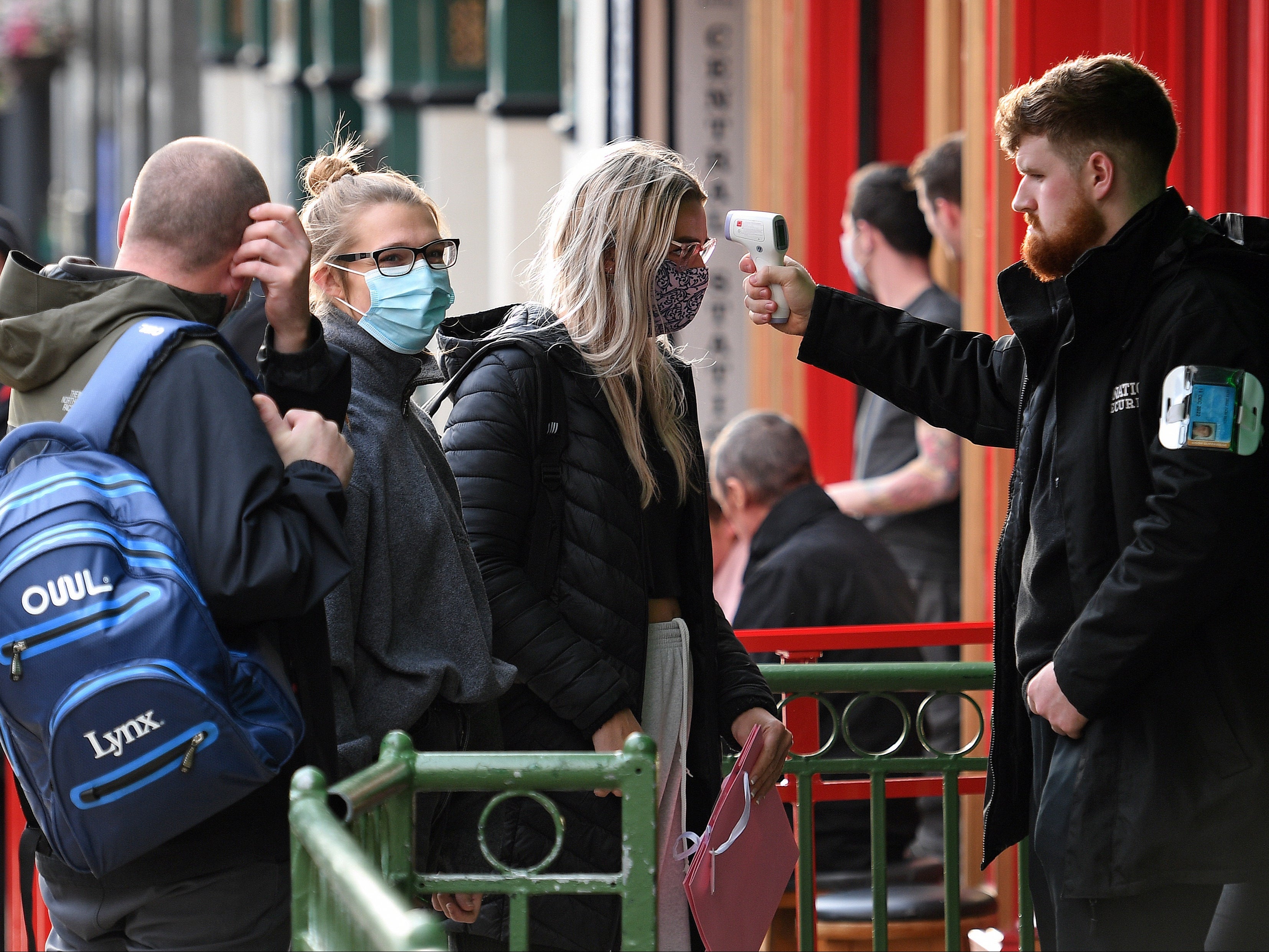 A security guard uses a handheld thermometer to take the temperature of customers as they wait to enter a bar in Liverpool