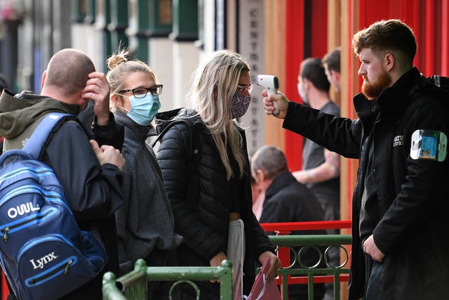 A security guard uses a handheld thermometer to take the temperature of customers as they wait to enter a bar in Liverpool