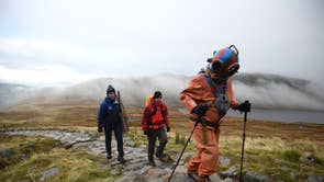 Veteran fundraiser Lloyd Scott, who is attempting to climb the Three Peaks whilst wearing a deep sea diving suit, is followed by members of his support team during his challenge on Ben Nevis in Scotland