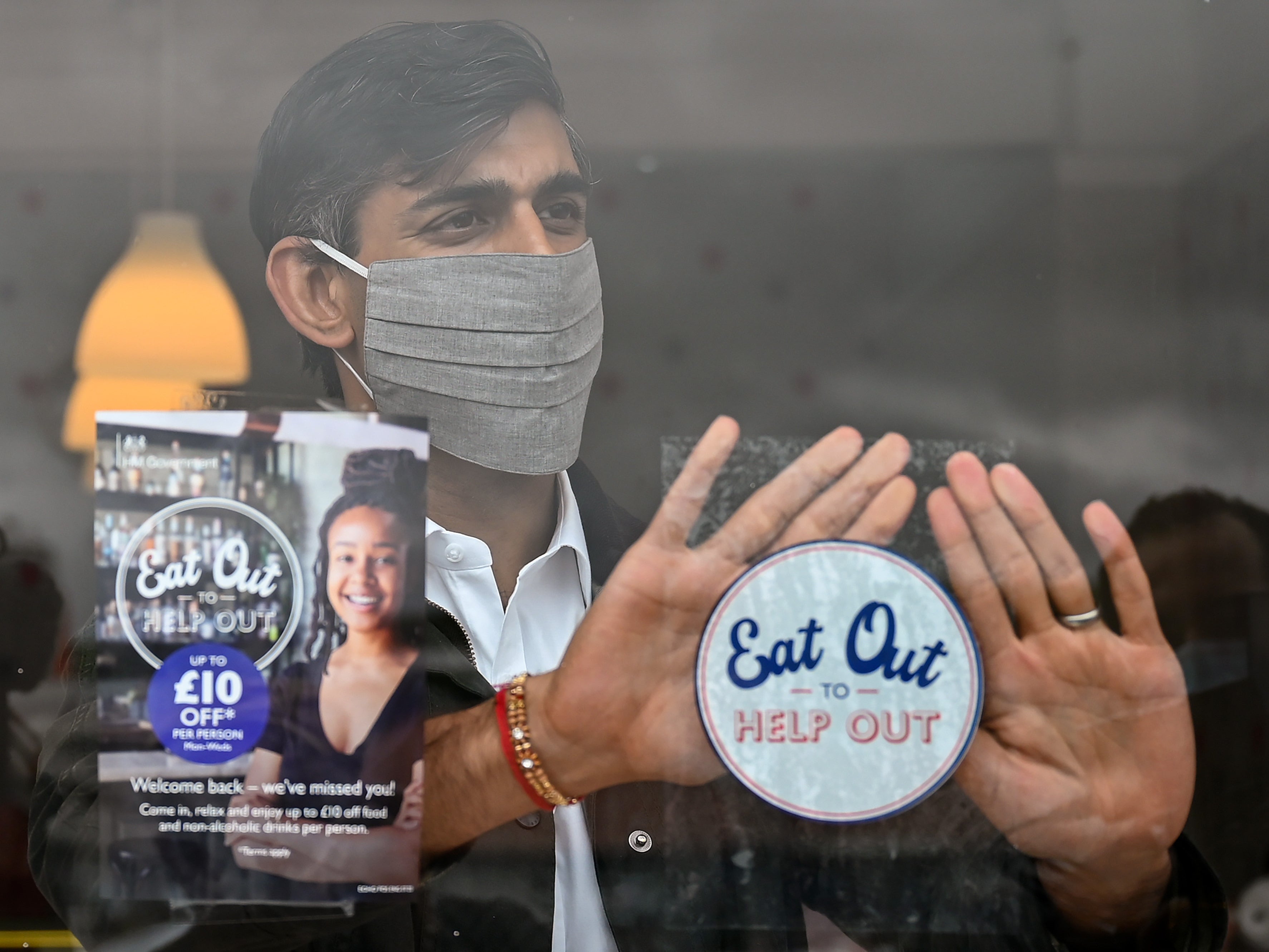 Rishi Sunak places an Eat Out to Help Out sticker in the window of a business during a visit to Rothesay on the Isle of Bute, Scotland