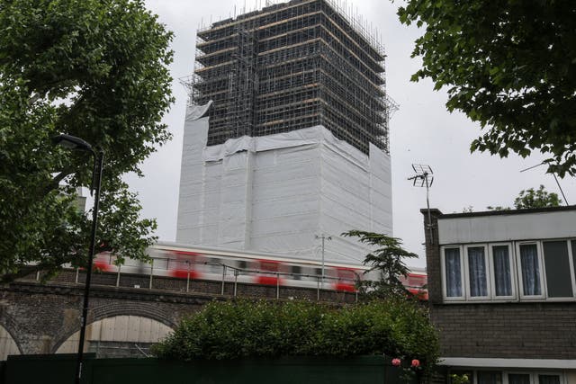 <p>A tube train passes the burned-out shell of Grenfell Tower block in west London on May 25, 2018.</p>