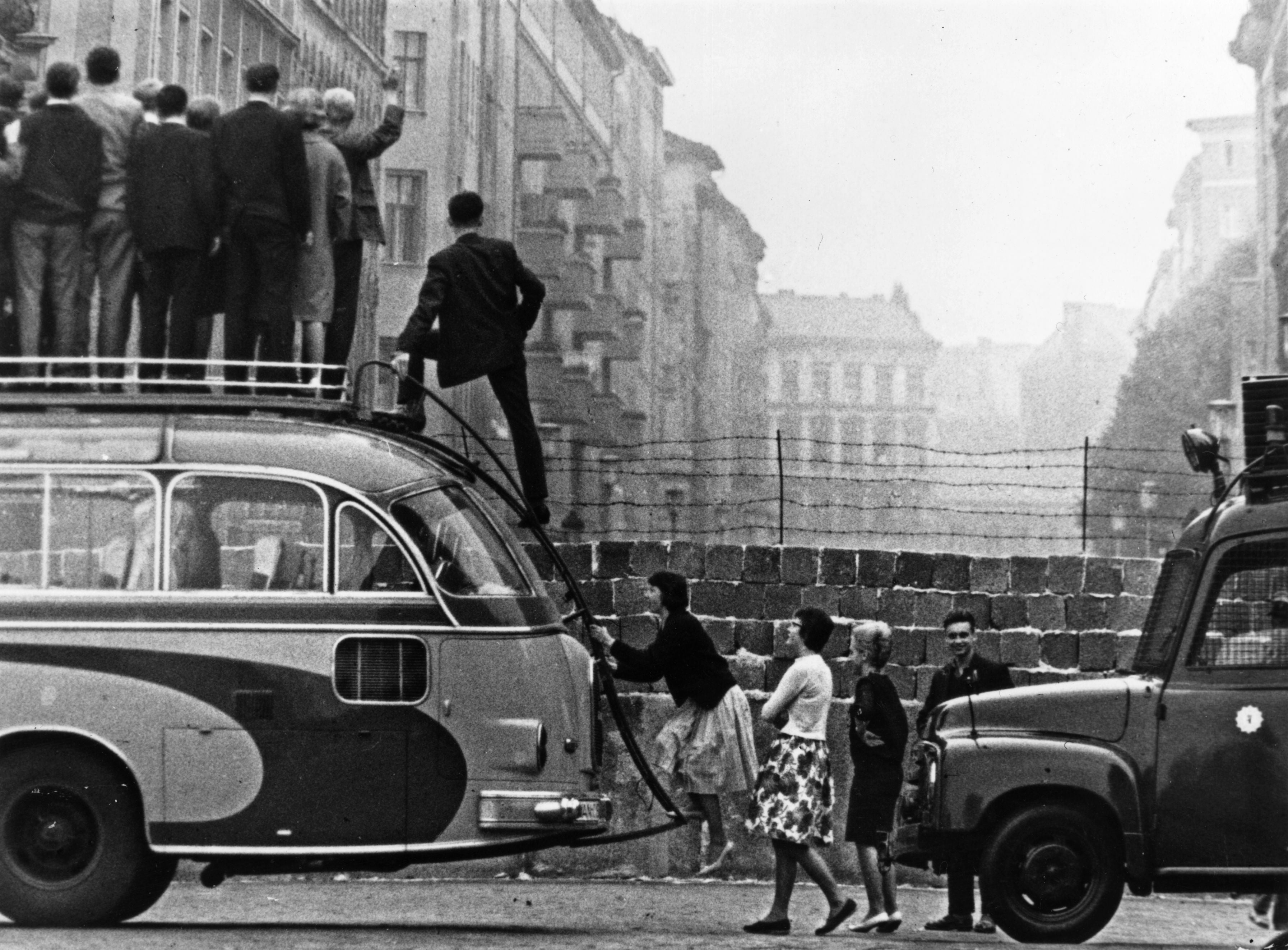 Sightseers climb onto a bus to look at the newly-built Berlin Wall in 1964