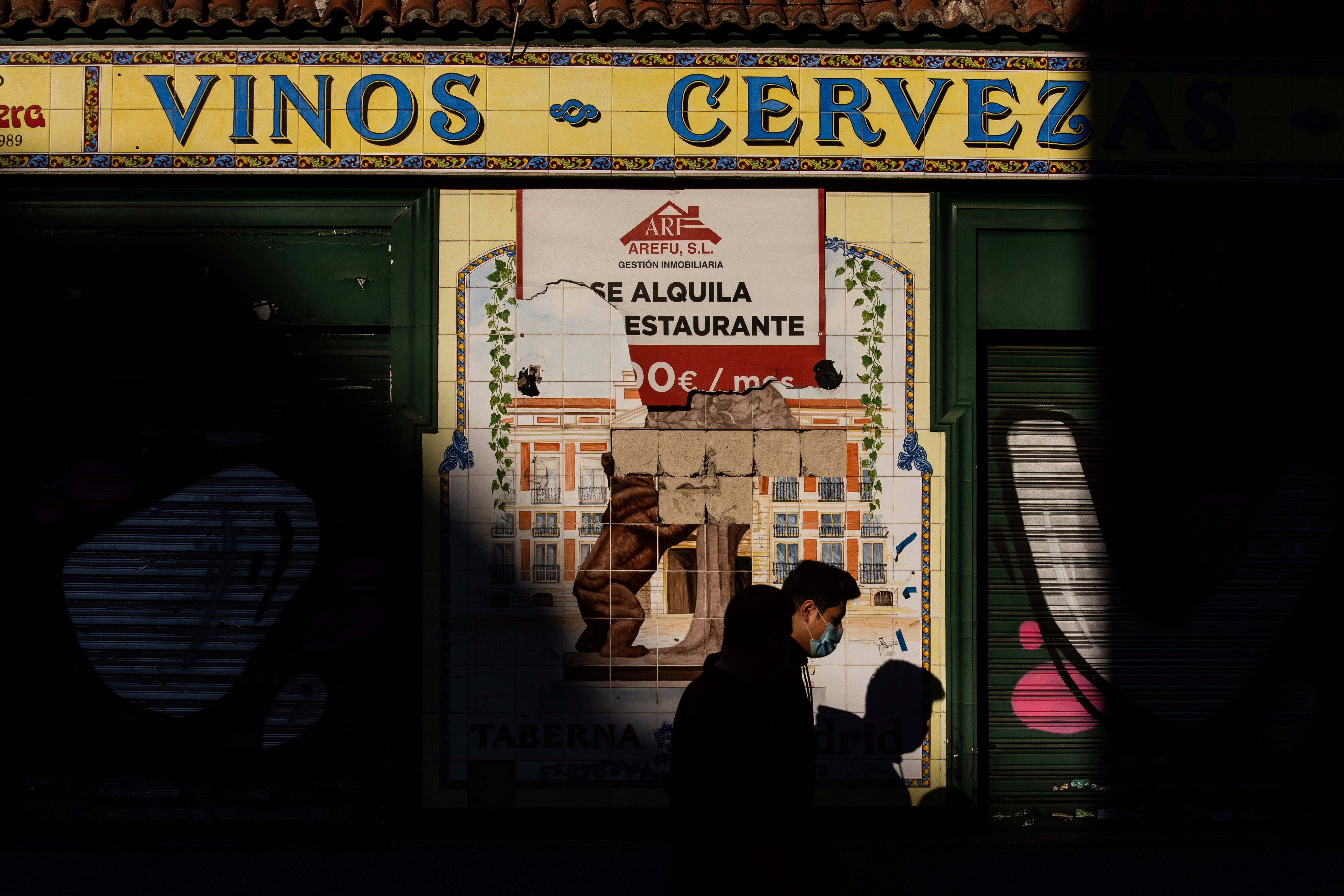 A man wearing a face mask to prevent the spread of the coronavirus walks past a closed business in Madrid, Spain. (AP Photo/Bernat Armangue)