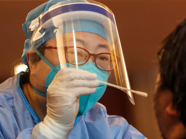 A medical worker wearing a full protective outfit swabs the throat of a journalist during a Covid-19 disease test in a Beijing hotel