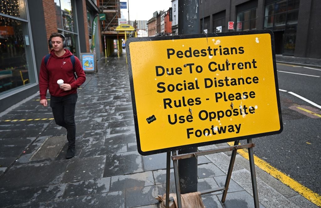 A pedestrian walks past a street sign in Liverpool reminding members of the public to adhere to social-distancing guidelines