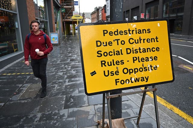 A pedestrian walks past a street sign in Liverpool reminding members of the public to adhere to social-distancing guidelines