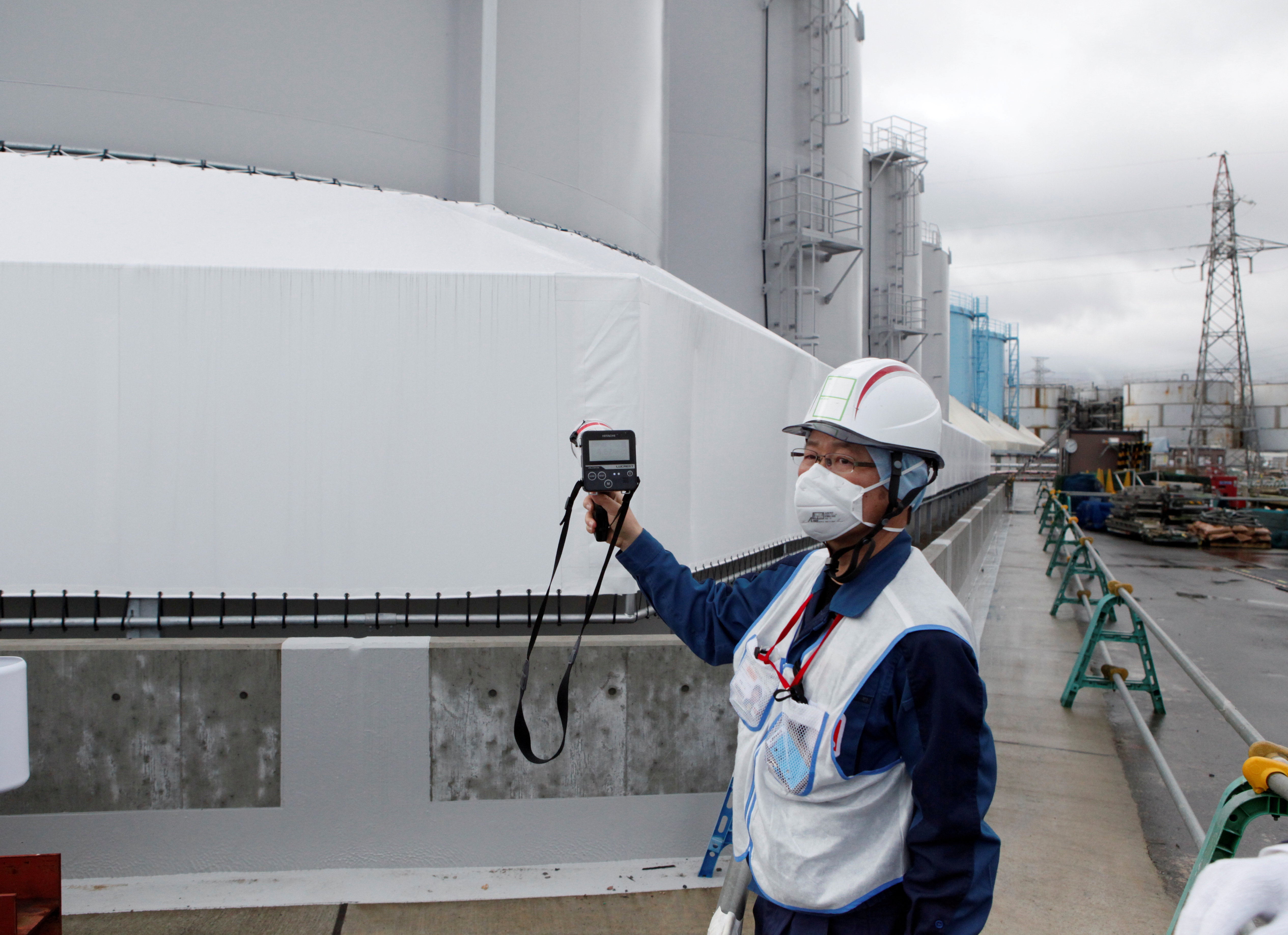An employee of Tokyo Electric Power Co (TEPCO) uses a geiger counter next to storage tanks for radioactive water at TEPCO's tsunami-crippled Fukushima Daiichi nuclear power plant in Okuma town, Fukushima prefecture, Japan,