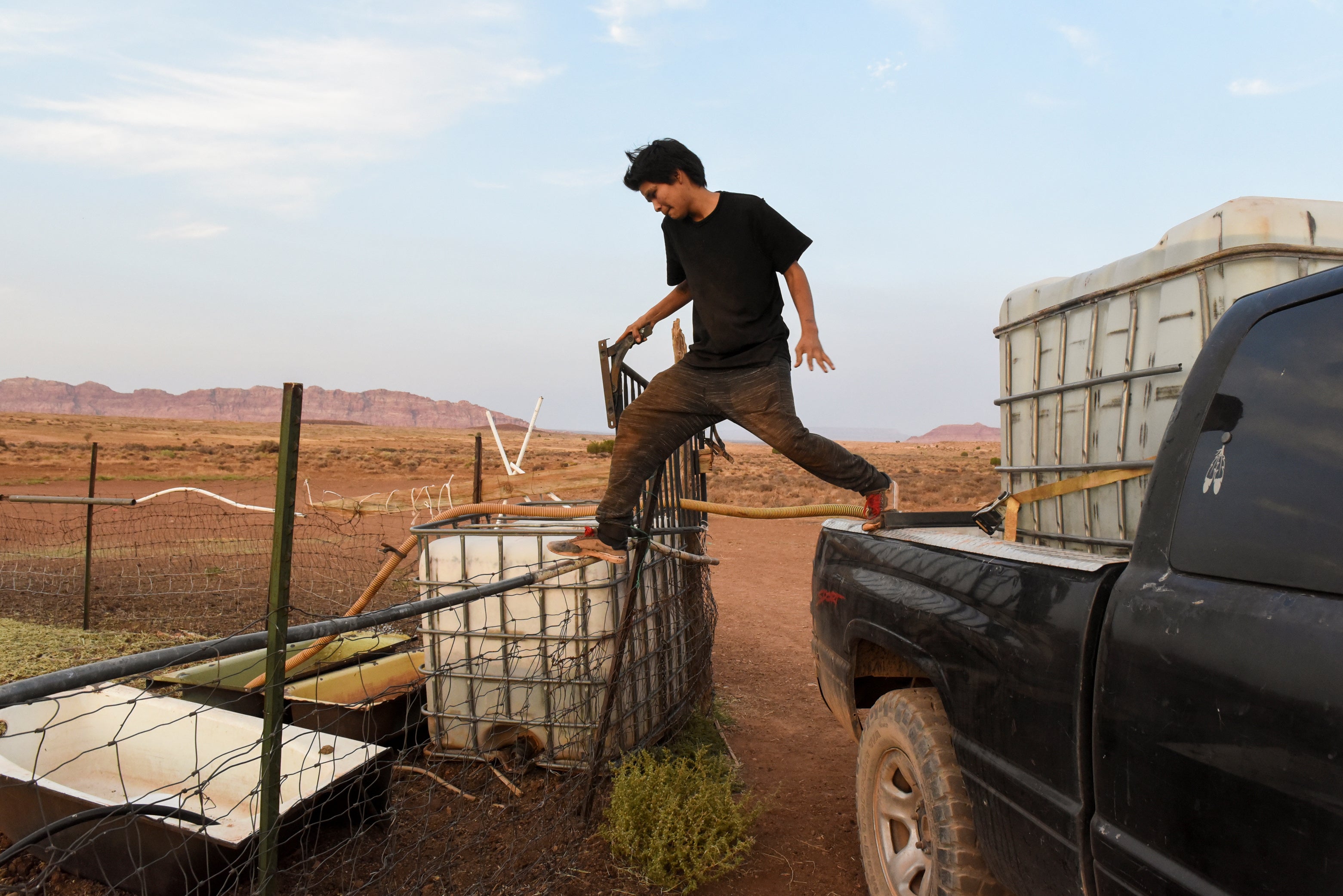 Tyson Boone, 16, steps from the back of a truck on to a fence in between two water containers