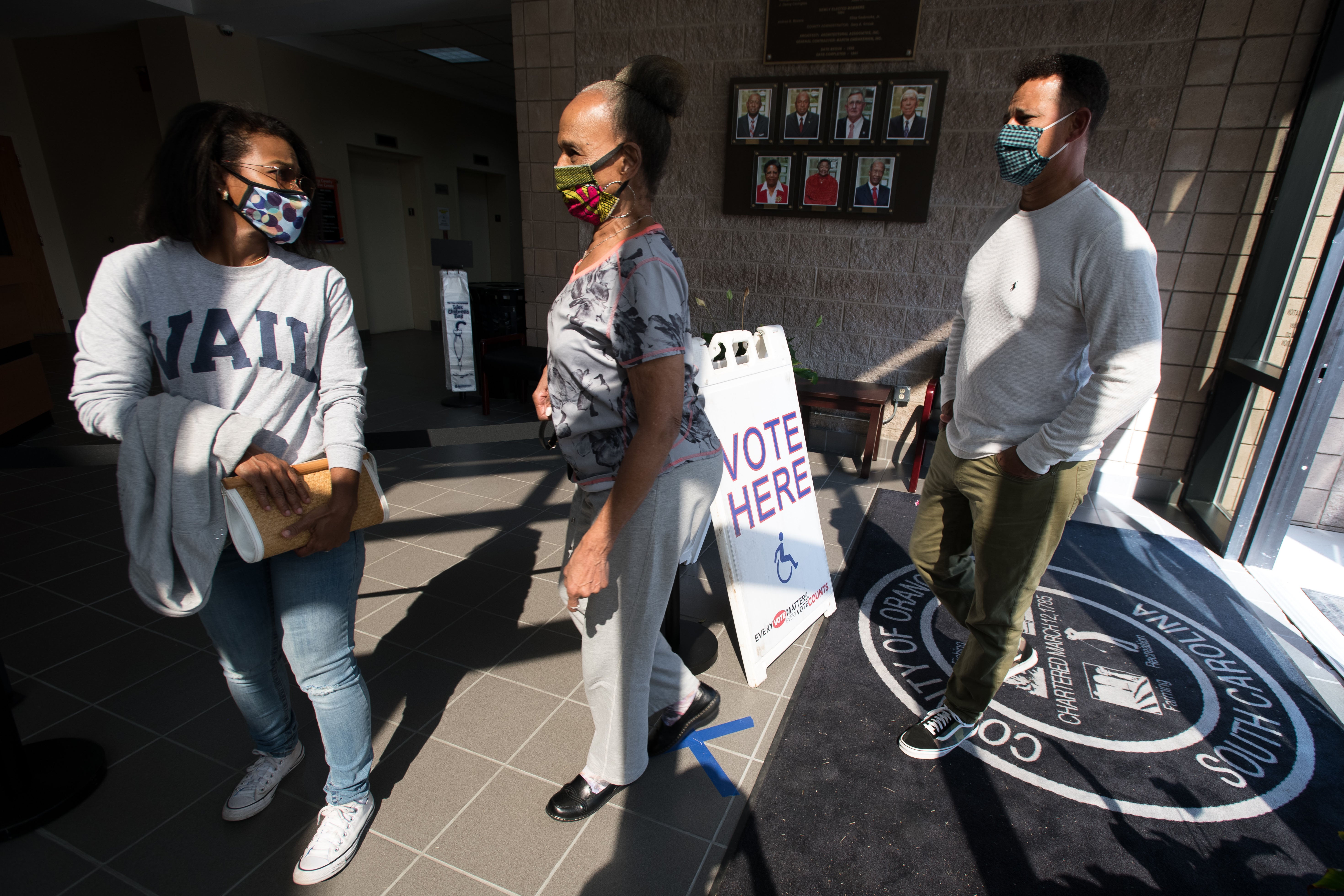 Kimberly Roache, left, Geneva Roache and Martin Roache stand in line to cast ballots at the Richland County Voter Registration and Elections Office in Columbia, South Carolina, on the first day of in-person absentee voting on Monday
