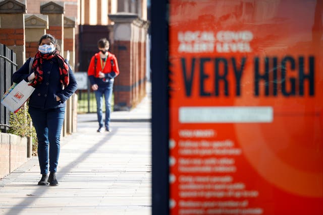 People wearing protective masks walk behind a covid warning sign in Liverpool