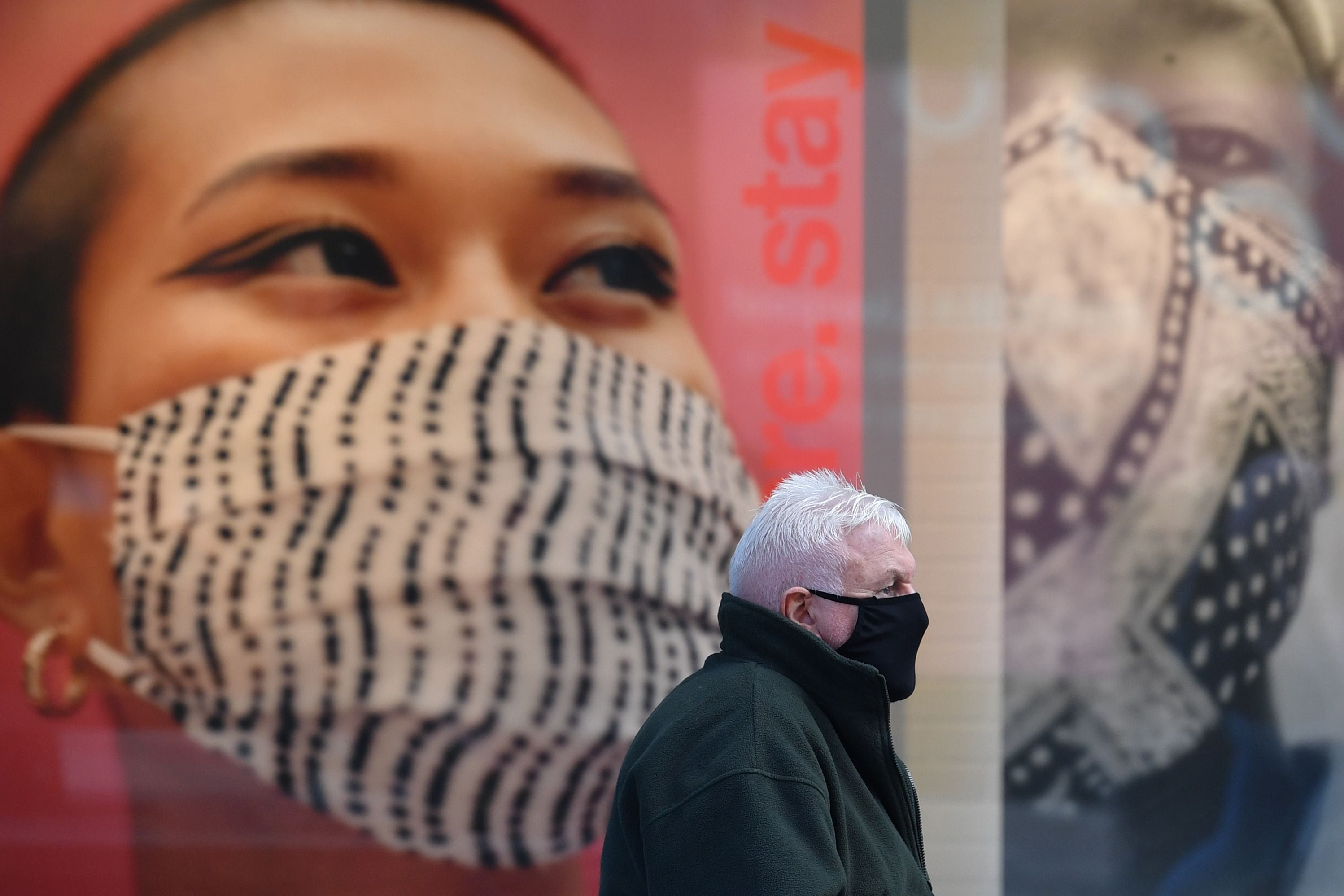 A pedestrian wearing a facemask sits by advertising for facemasks in central Liverpool, one of the regions under tier three measures