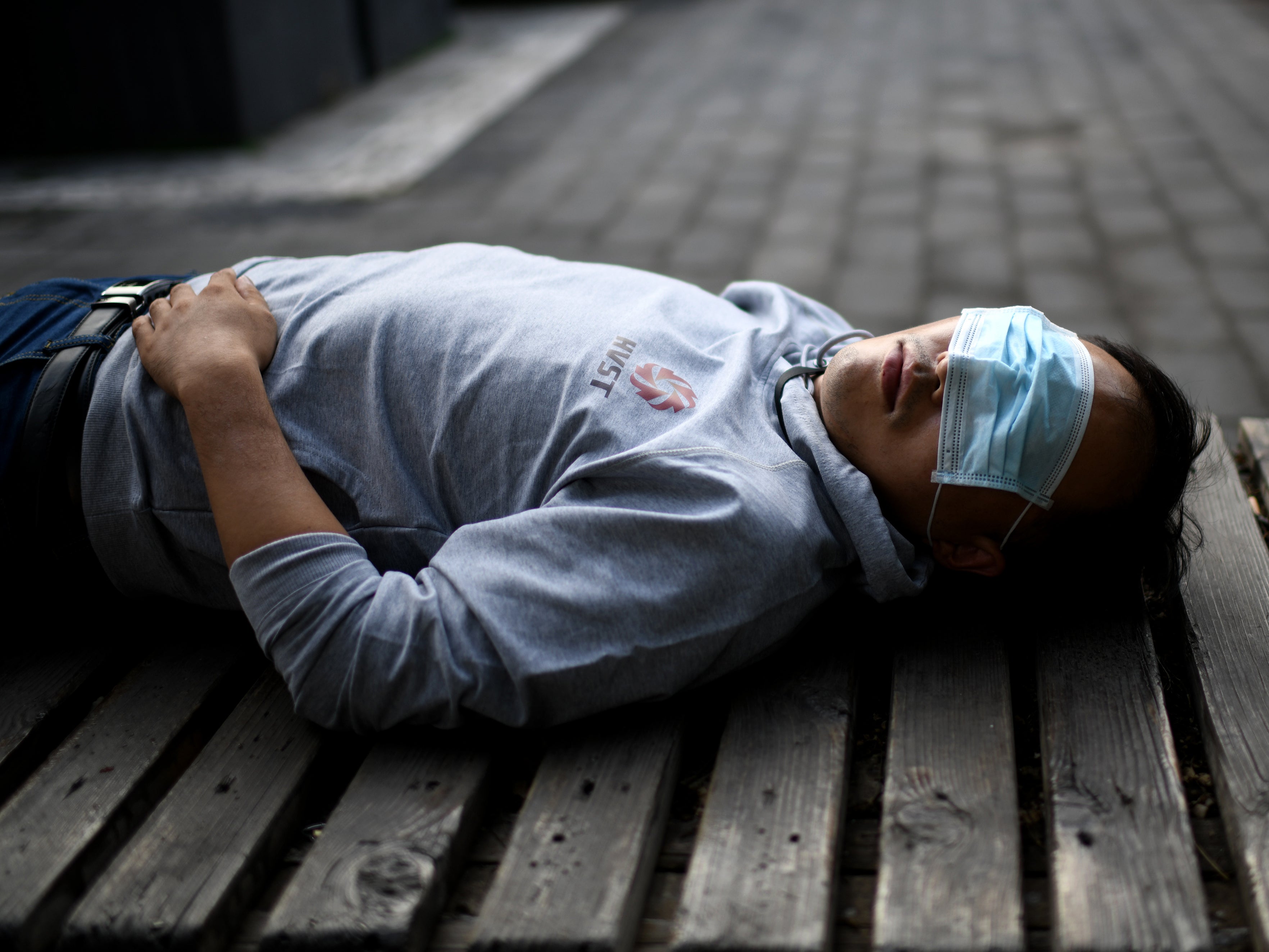 A man sleeps on a bench while wearing a face mask