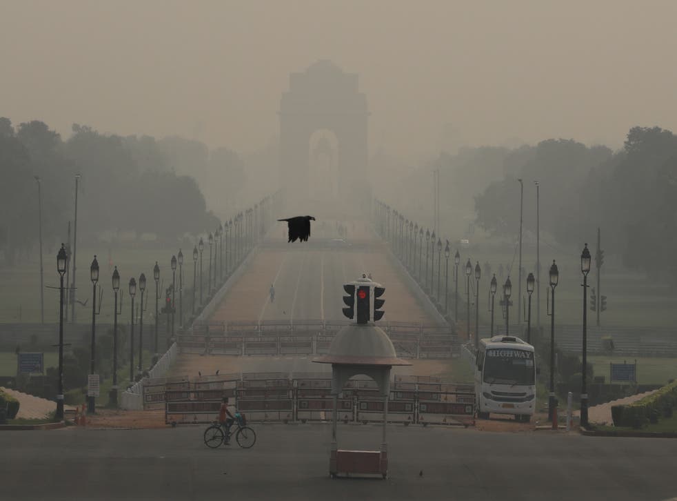 A man rides a bicycle on a hazy morning near India Gate in Delhi