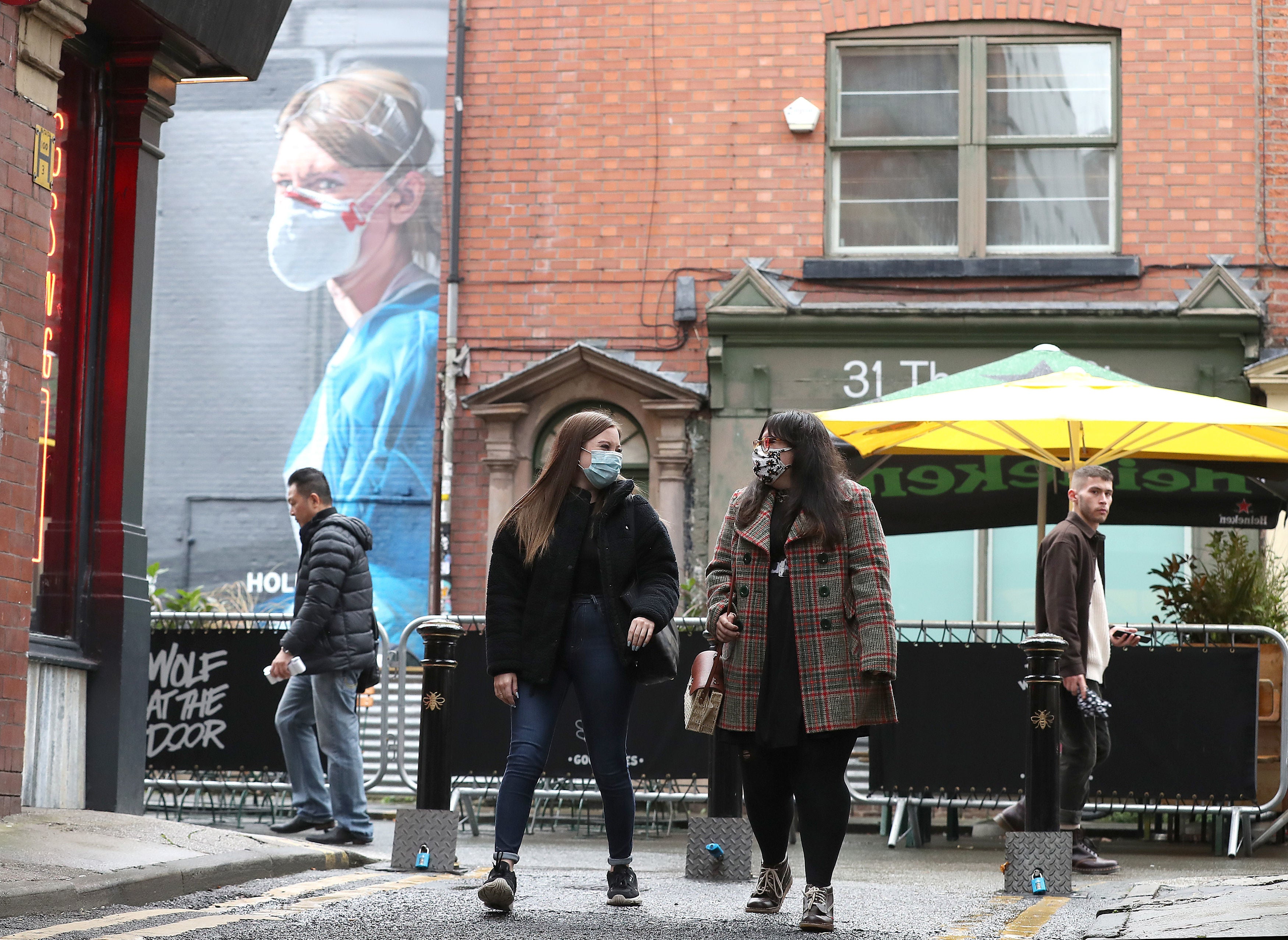 People wearing a face mask walk near a mural of a nurse in the Northern Quarter of Manchester