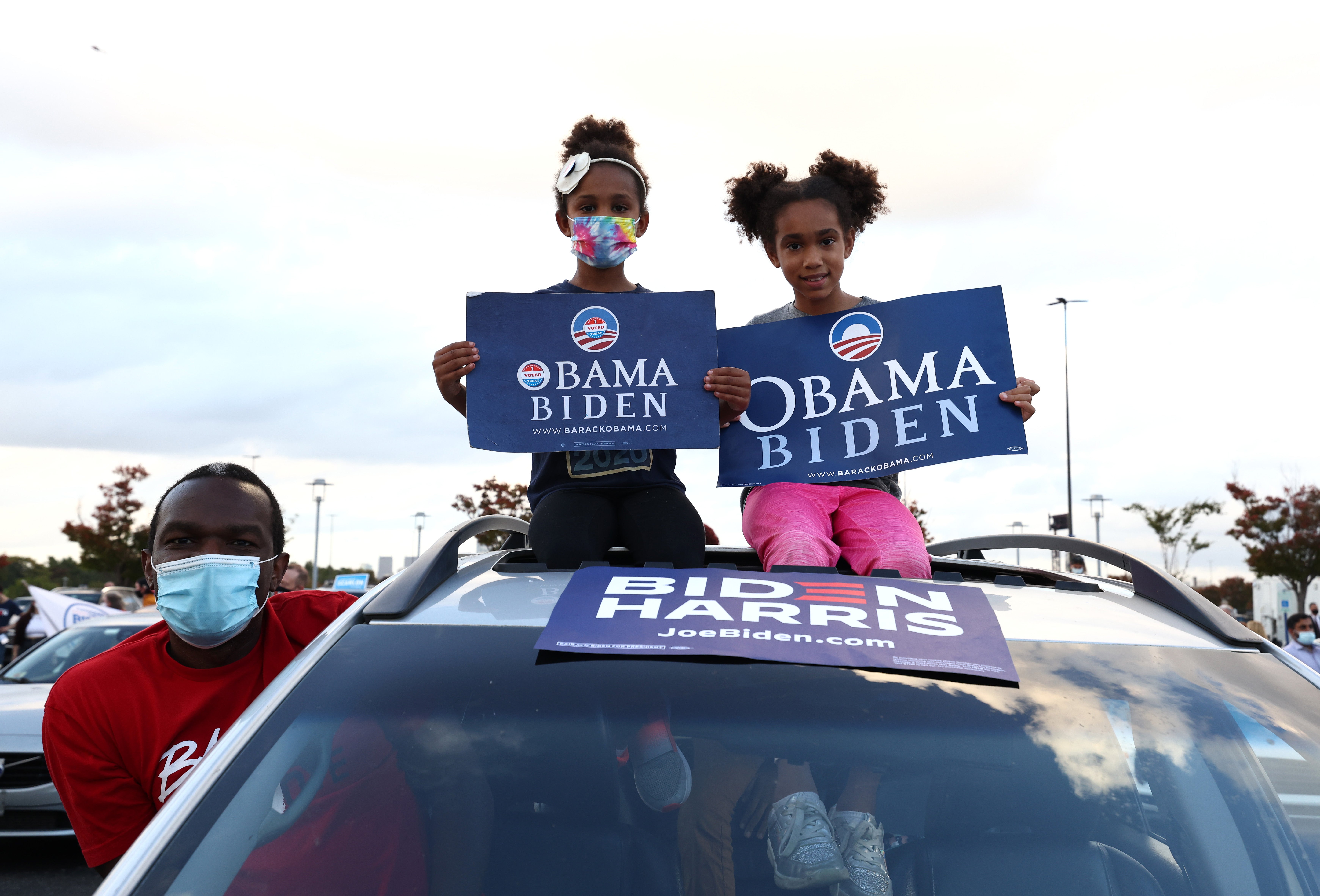 Sozi Tulante (L) and his two daughters Zolana 7, and Sengele 9, gather to listen to former President Barack Obama speak at a drive-in rally while he campaigns for Democratic nominee and former Vice President Joseph Biden on October 21, 2020 in Philadelphia, Pennsylvania. Today is the first in-person campaigning for former President Barack Obama who is campaigning for the Biden Harris ticket. (Photo by Michael M. Santiago/Getty Images)