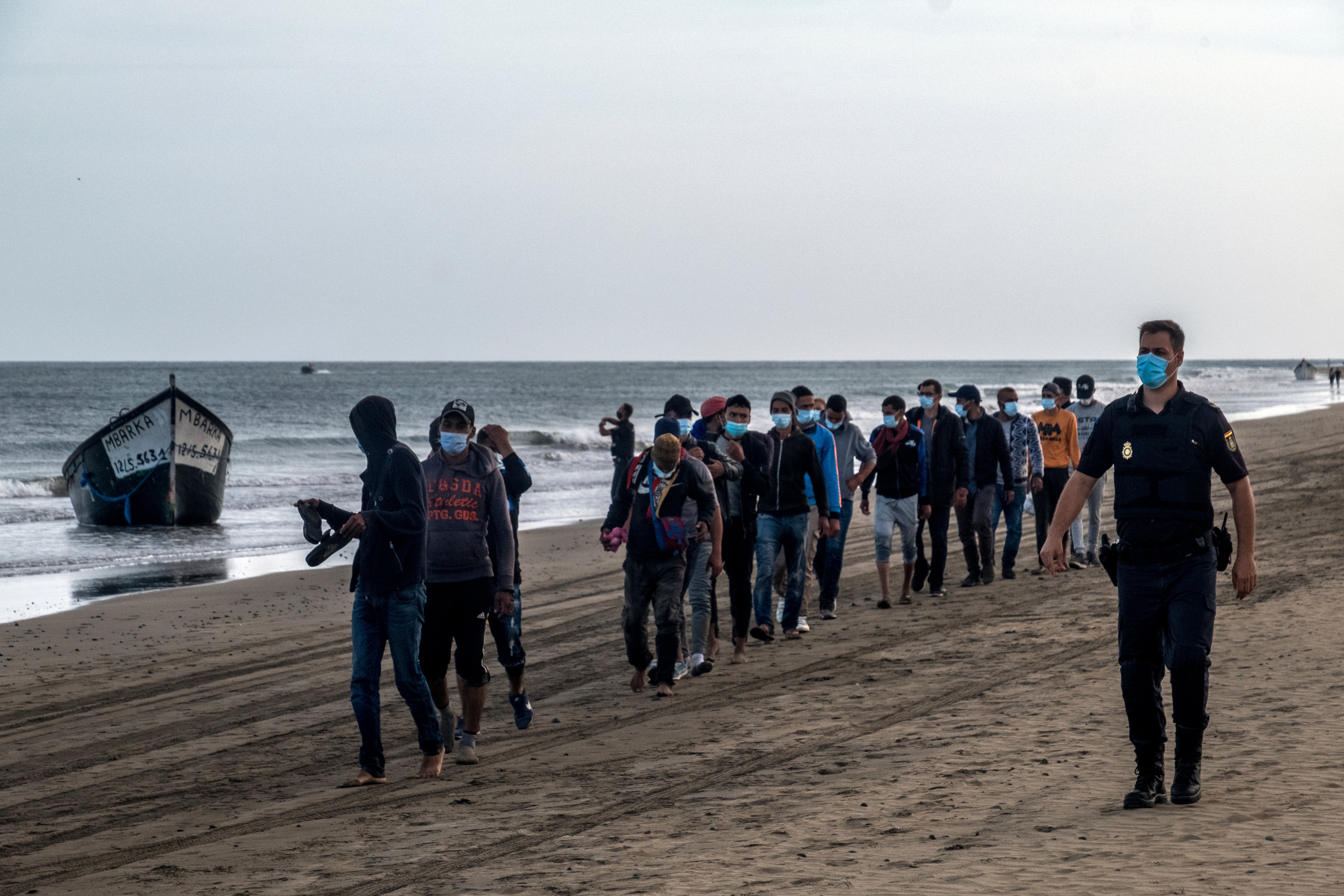 Migrants from Morocco walk along the shore escorted by Spanish Police after arriving at the coast of the Canary Island, crossing the Atlantic Ocean sailing on a wooden boat on Tuesday, Oct.20, 2020. (AP Photo/Javier Bauluz)