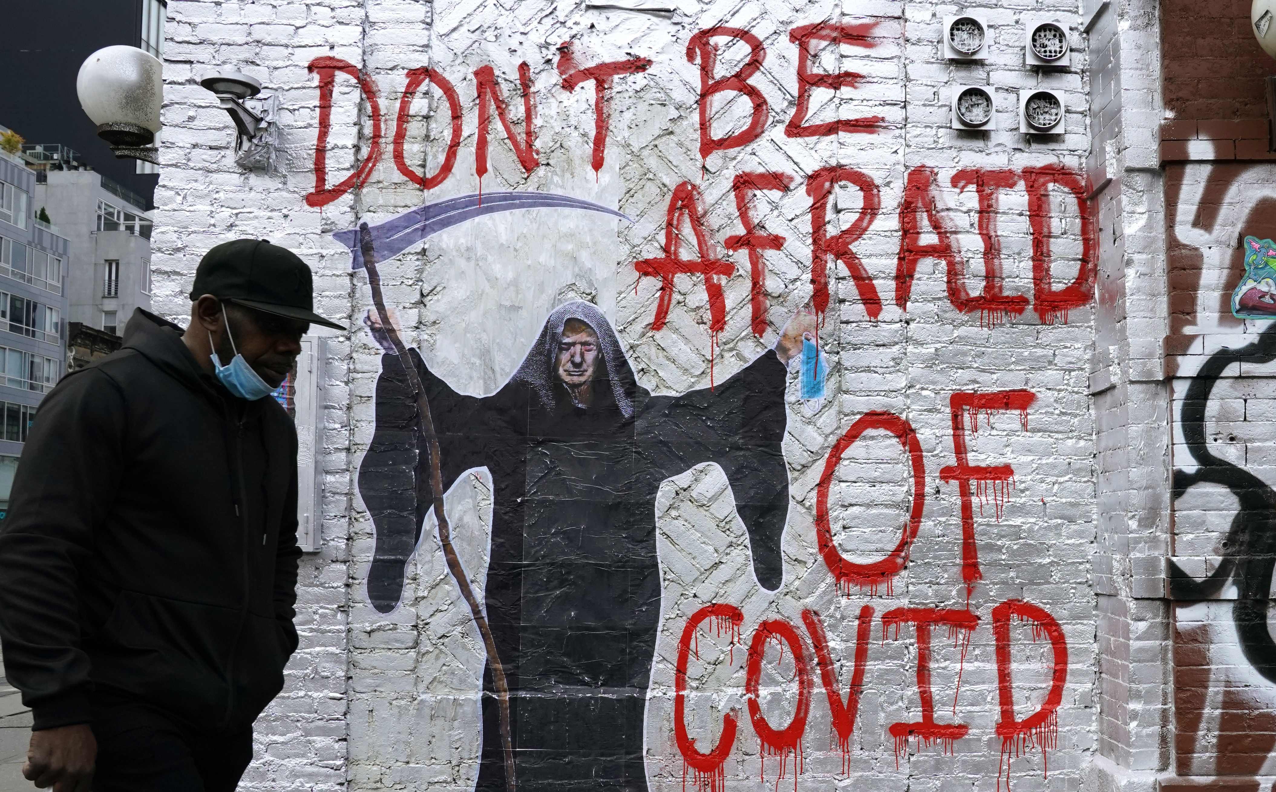A man walks past a mural by the artist who goes by the name "Pure Genius" depticting US President Donald Trump as the Grim Reaper on a wall on Houston Street in New York City