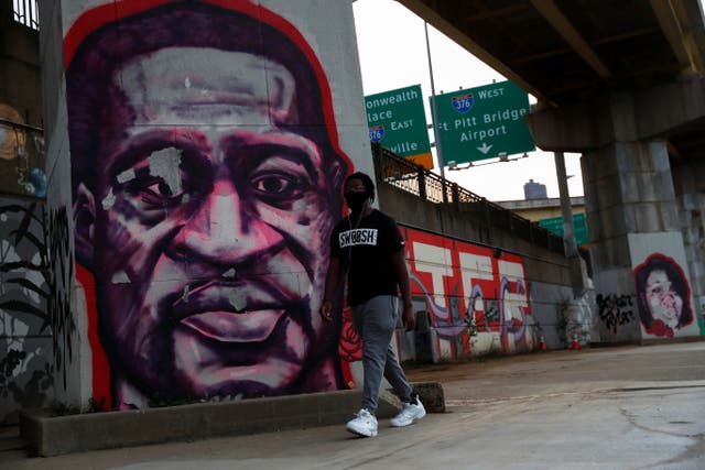 <p>A man wearing a protective face mask walks by murals of George Floyd and Breonna Taylor in Pittsburgh</p>