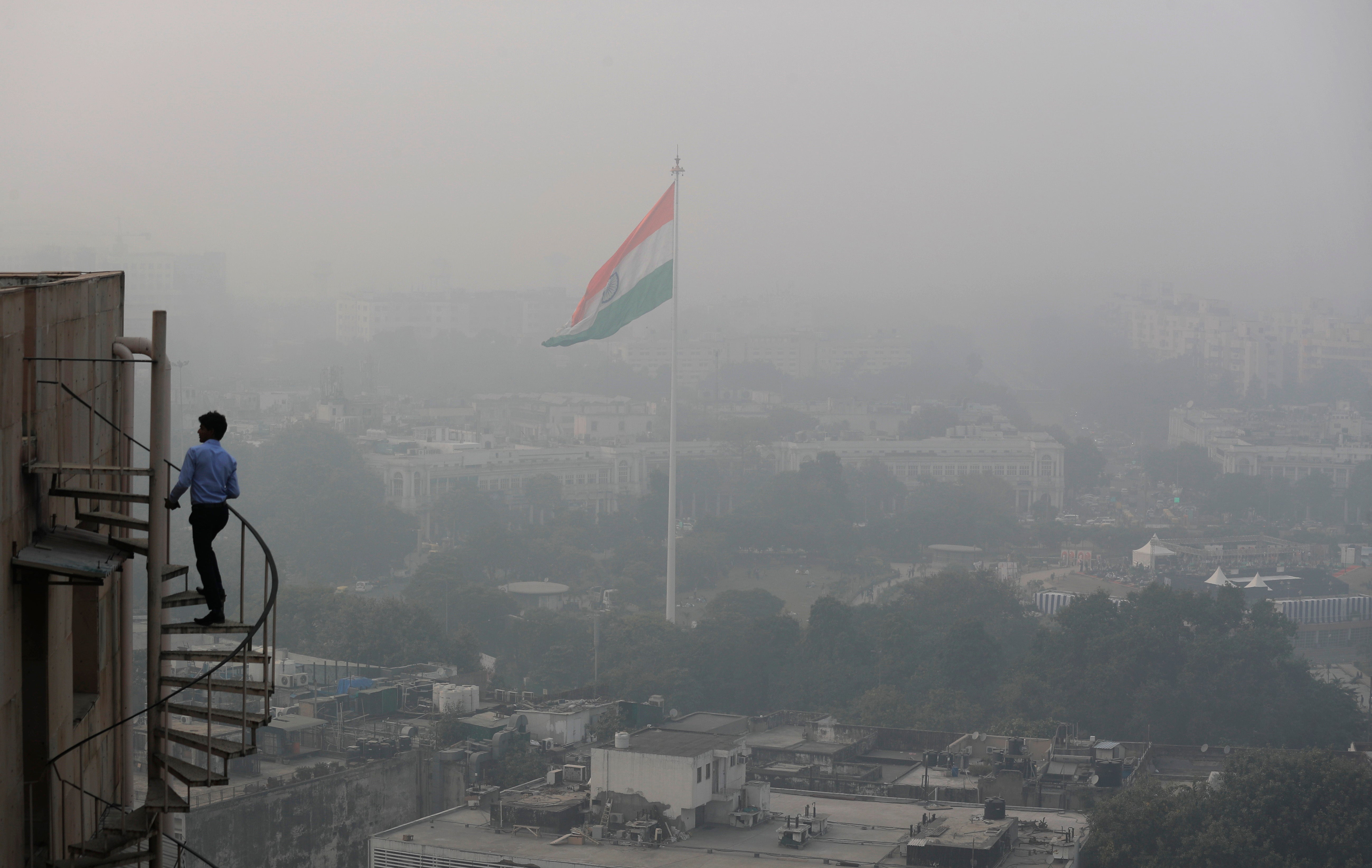 An Indian man walks up stairs as Delhi’s skyline is seen enveloped in smog and dust