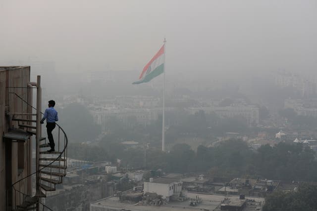 An Indian man walks up stairs as Delhi’s skyline is seen enveloped in smog and dust
