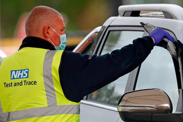 A driver receives a Covid-19 self-test kit from a worker wearing an NHS Test and Trace branded Hi-Vis jacket at a drive-in testing facility in Chessington