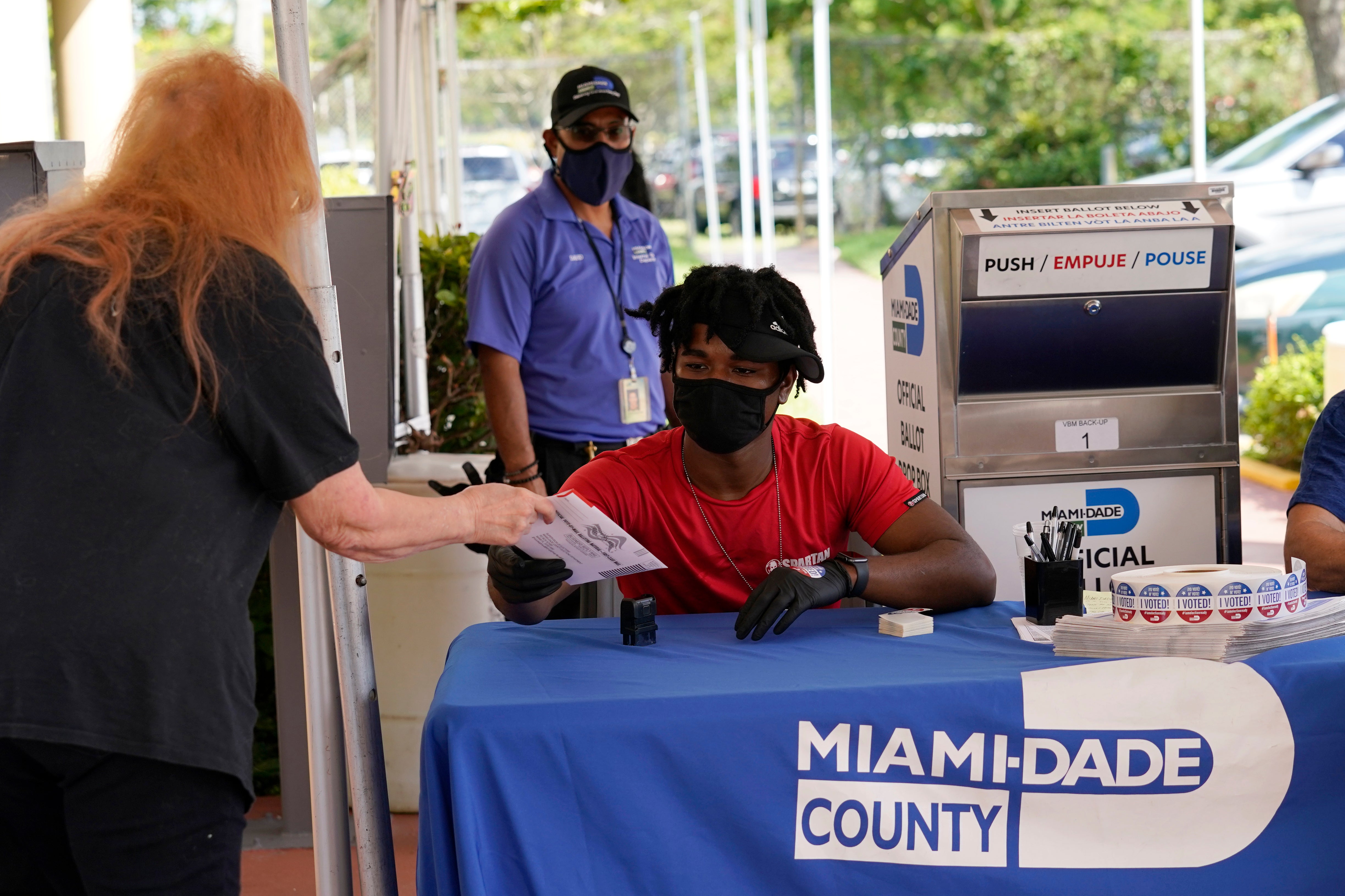Election worker Najeh Fisher, right, takes a vote-by-mail ballot to place into an official ballot drop box at the Miami-Dade County Elections Department on 14 October in Florida.