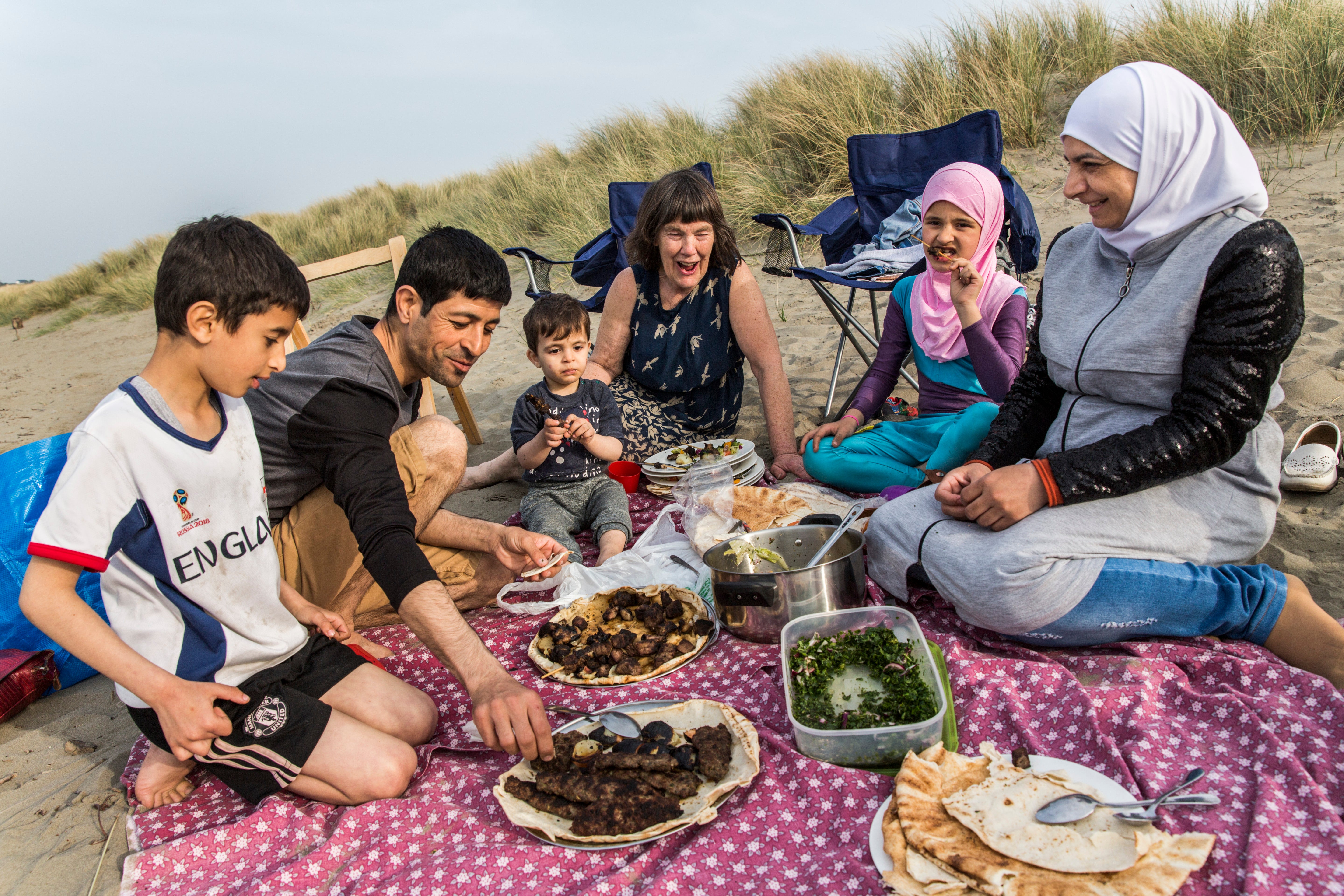 Vicky Moller (centre) has a picnic at a beach in south Wales with the Alchik family, Muhaned, his wife Naheda, and their children (from left) Shadi, 8, Hadi, 1, and Sara, 9, who fled their home during the war in Syria