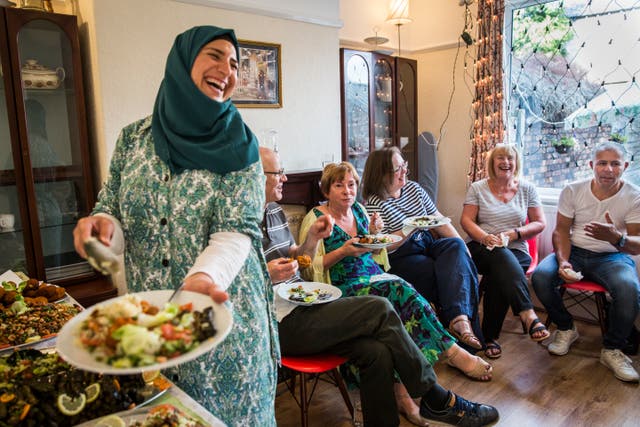<p>Ghofran Khaled Jhayem (left) and her husband Ismael share Syrian food with members of their community support group at the family's new home in Liverpool</p>