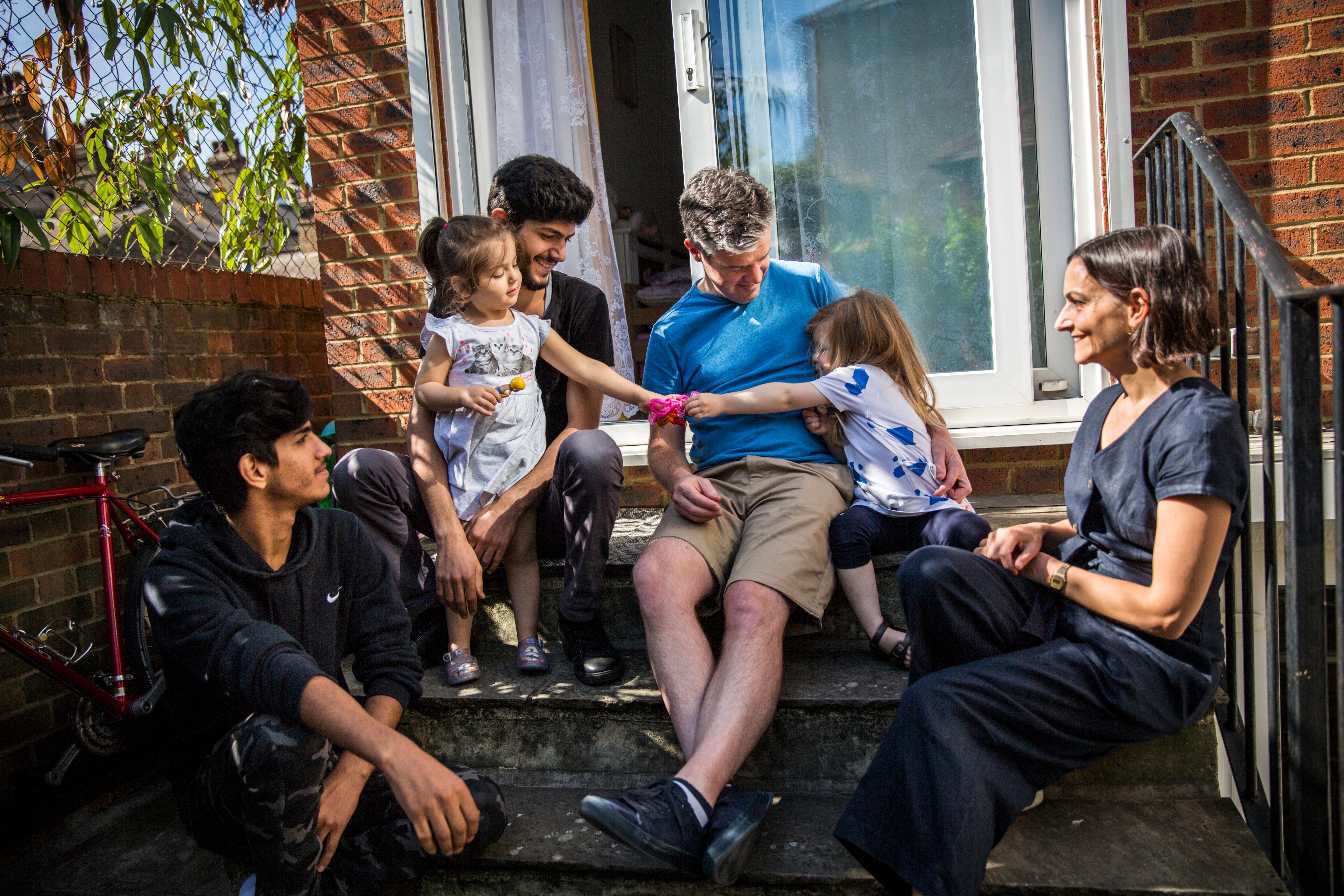James Lynch (in blue), his daughter, and Claire Tillotson (right), from the Peckham Sponsors Refugees local residents group, socialise with Mohammed Al-Shaabin (top-left), his daughter Celen, and his brother Islam – all of whom fled Syria in 2011 – outside their home in south London