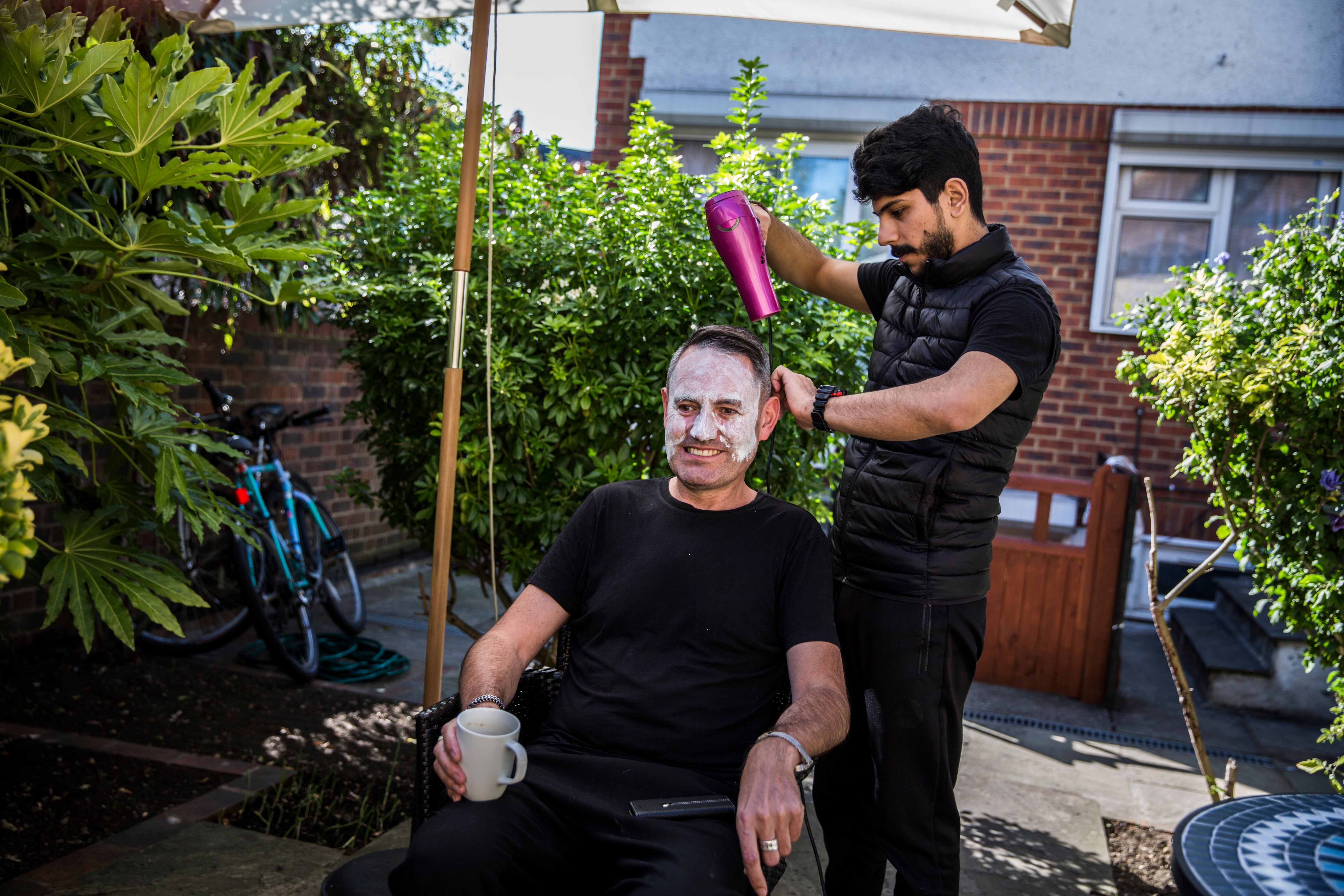 Syrian refugee Lutfi Al-Shaabin, who worked as a barber in Jordan where his family lived as refugees, cuts Tim Finch's hair at the Al-Shaabin home in south London