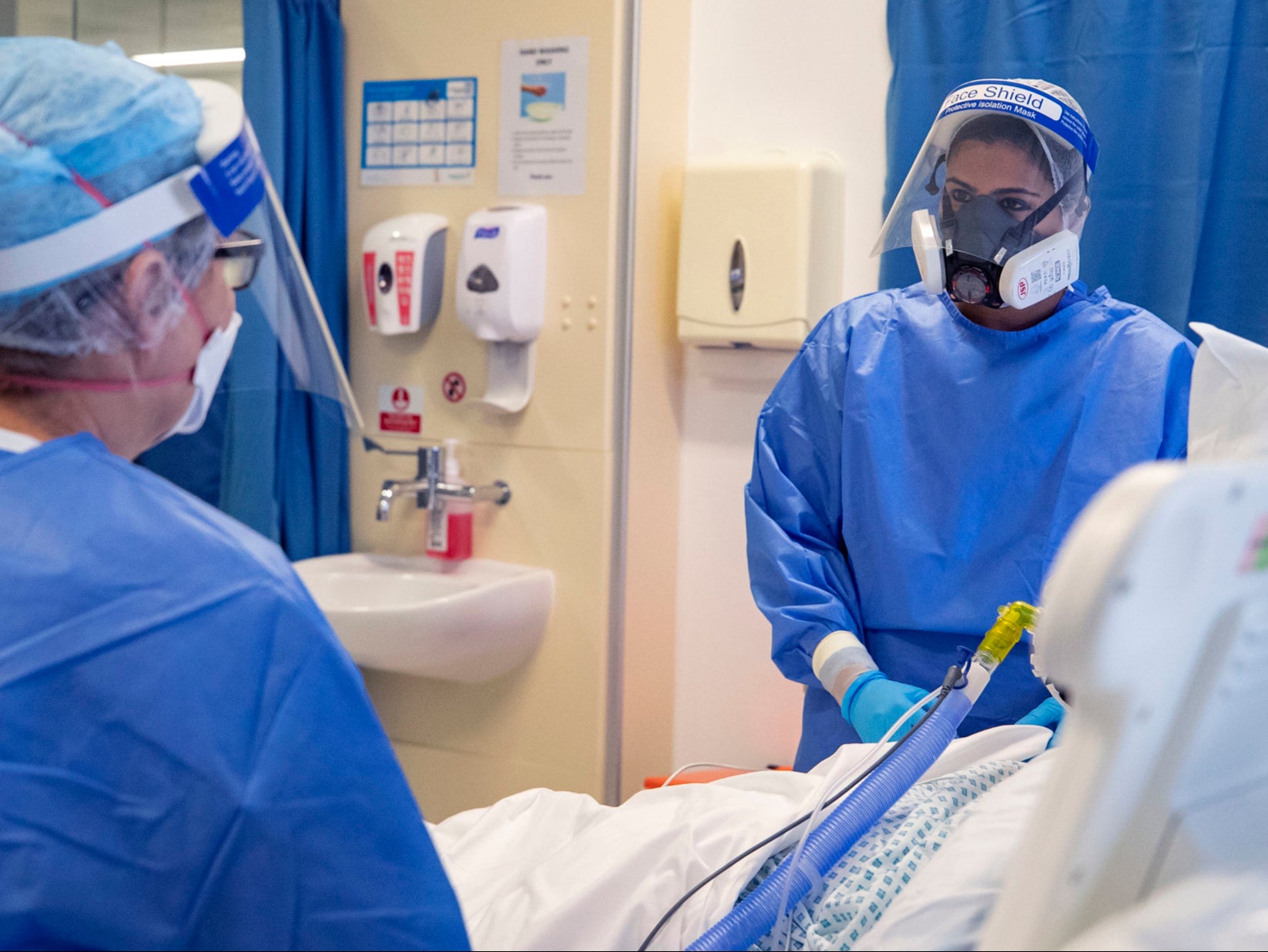 Health workers wearing full personal protective equipment tend to a patient on the intensive care unit at Whiston Hospital in Merseyside.