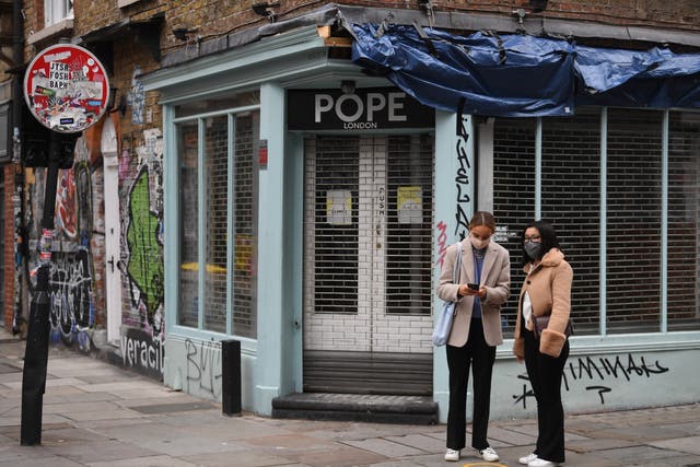 <p>Masked people pass a closed shop in London last month</p>